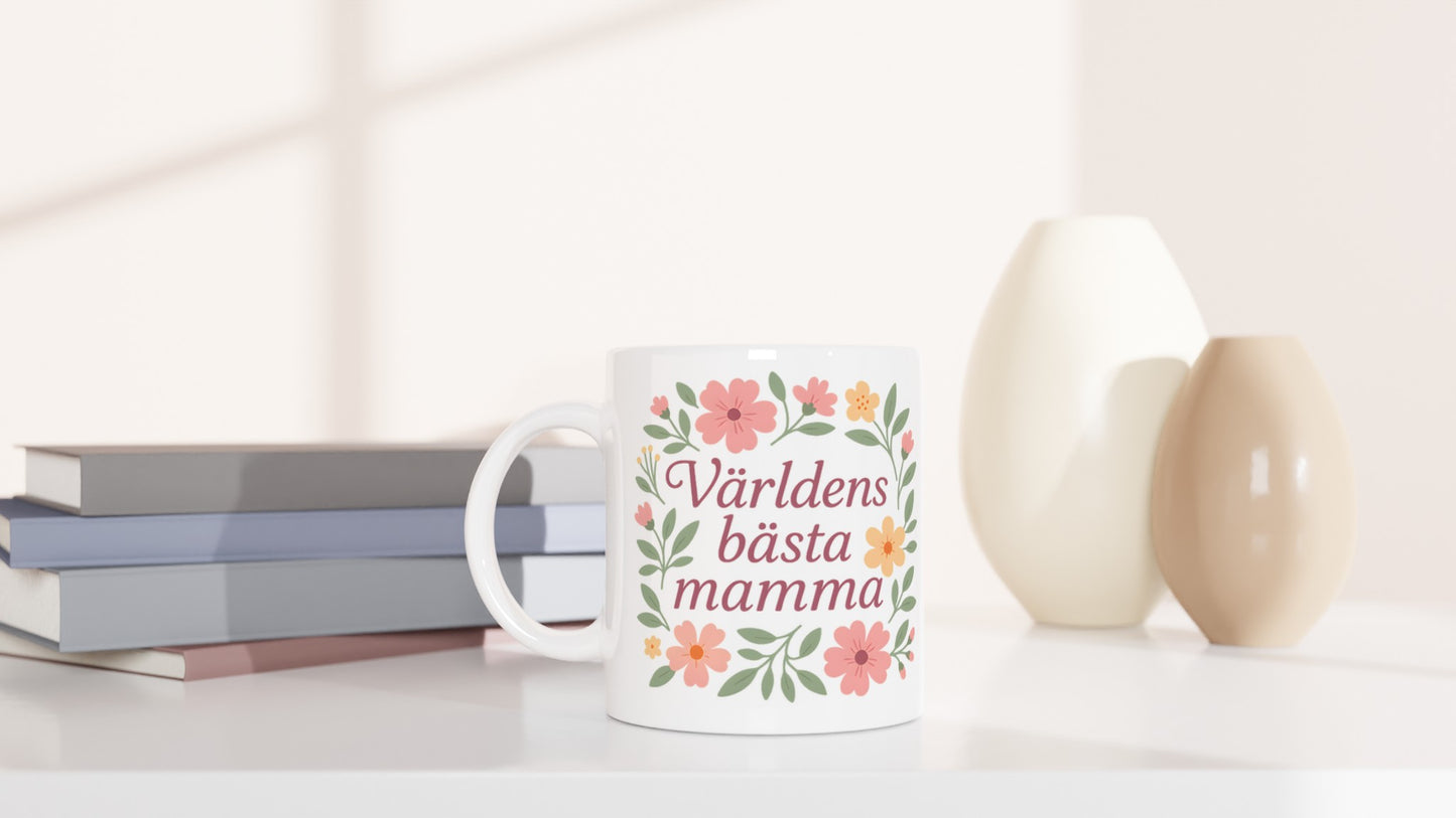 Mugg med texten Världens bästa mamma omgiven av mjuka blommor och blad i pastellfärger.